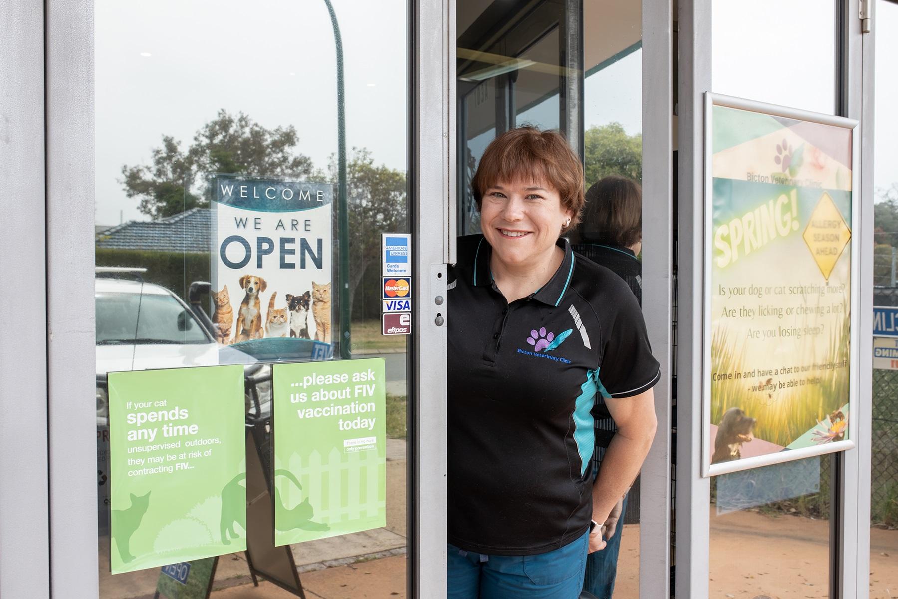Photo of a female business owner. She is standing in the entry to her business premises.