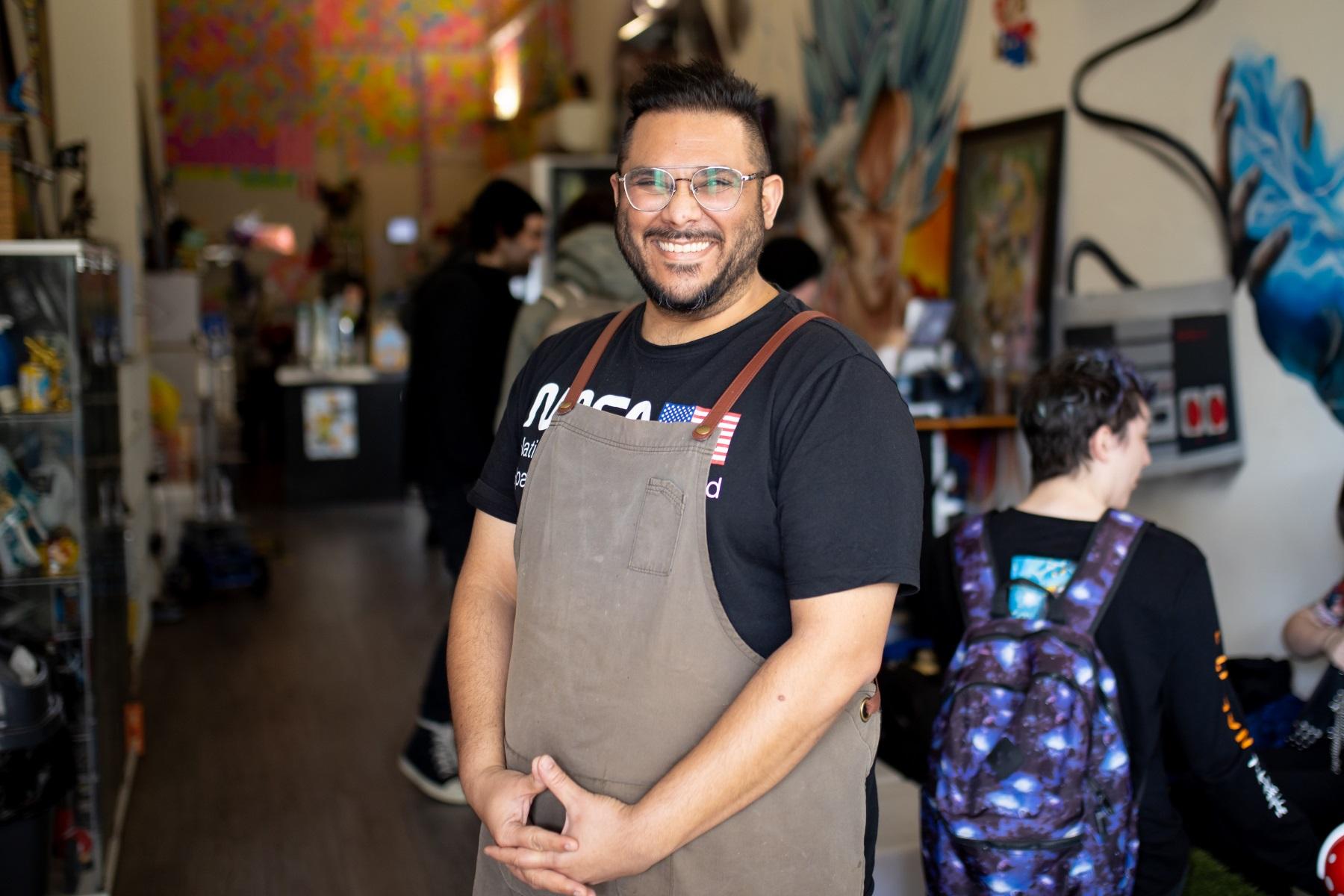 Photo of a male business owner standing at the entrance to his cafe. He is smiling at the camera.