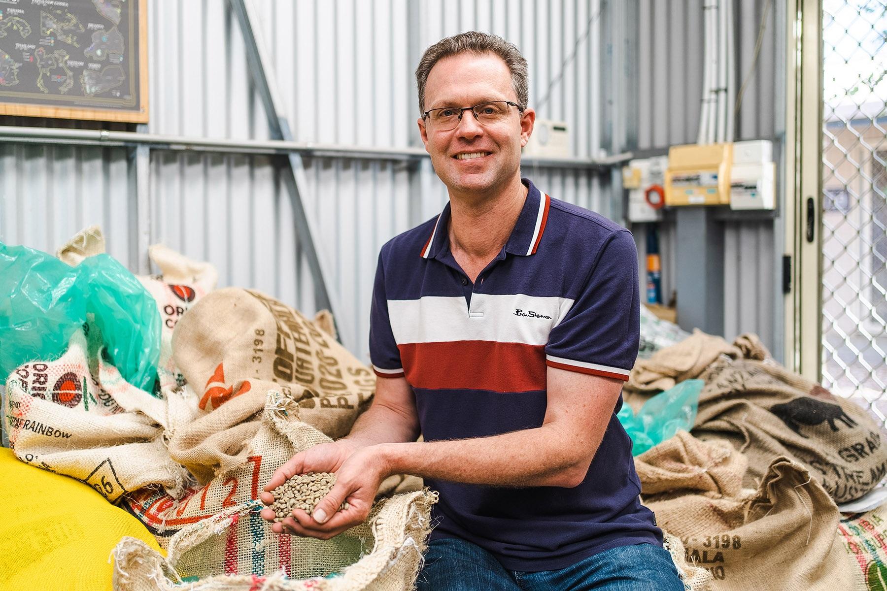 Photo of a male business owner. He is holding coffee beans in his coffee roasting facility.