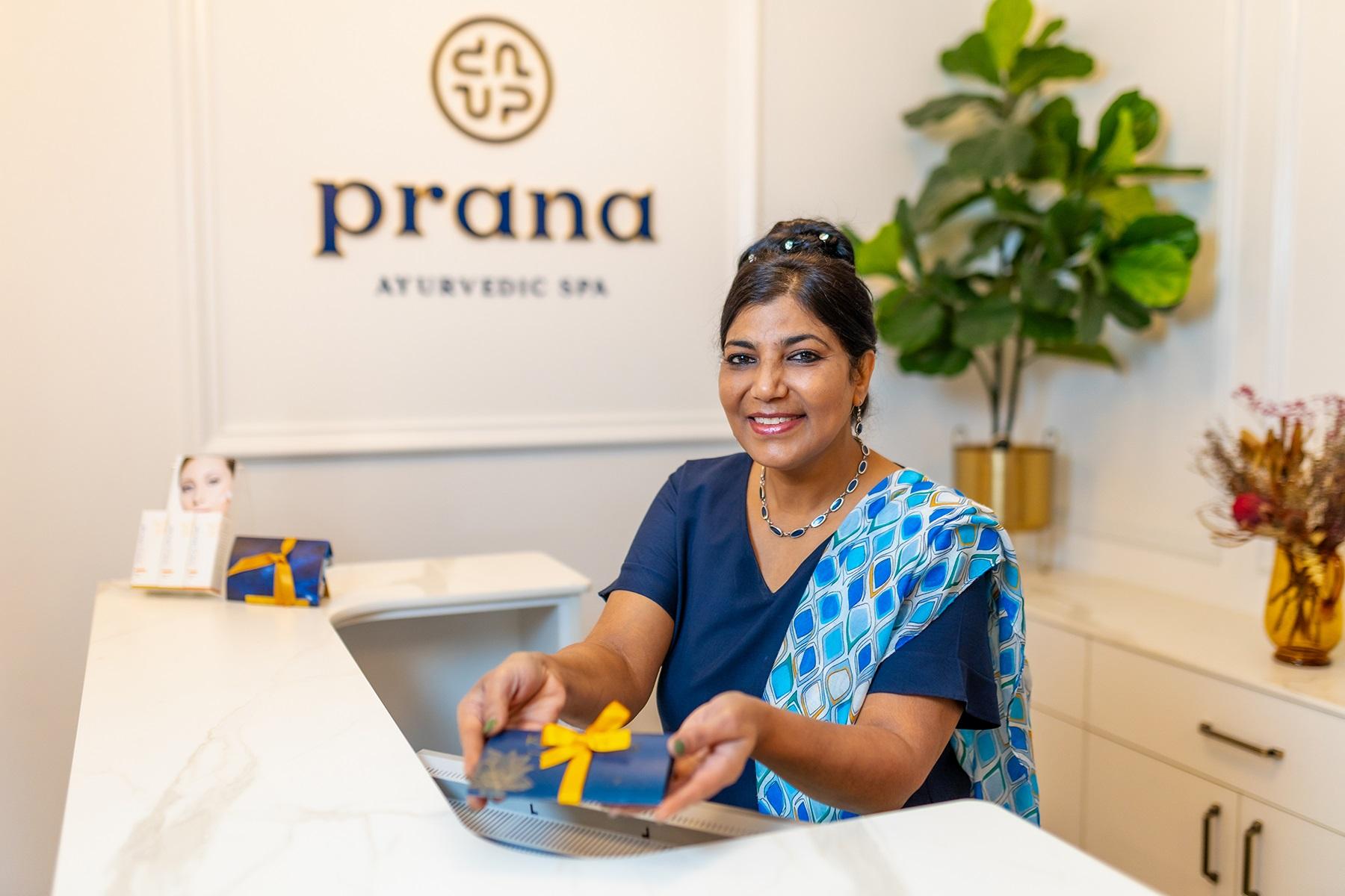 Photo of a female business owner. She is sitting at a reception desk holding a gift.