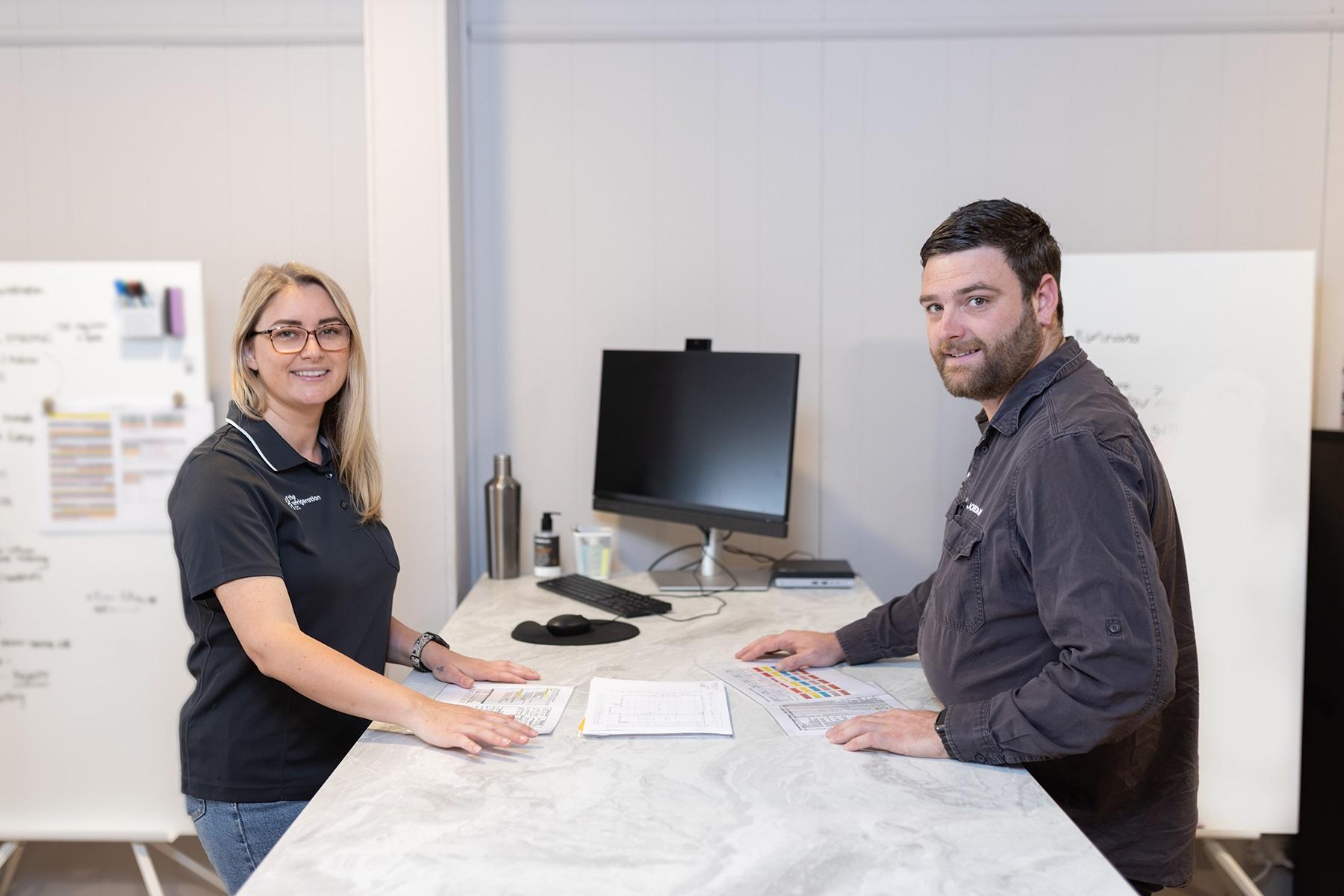 Photo of a woman and man standing at a desk. They are reviewing paper documents.