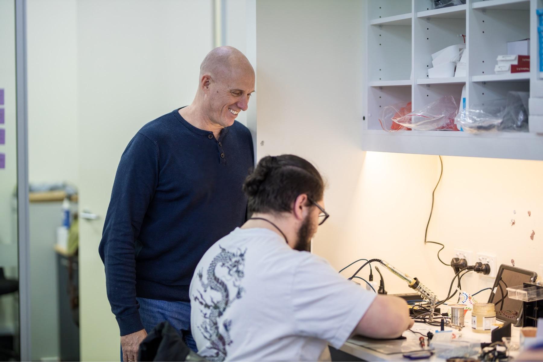 Photo of a business owner observing a staff member's work to repair a tech item.