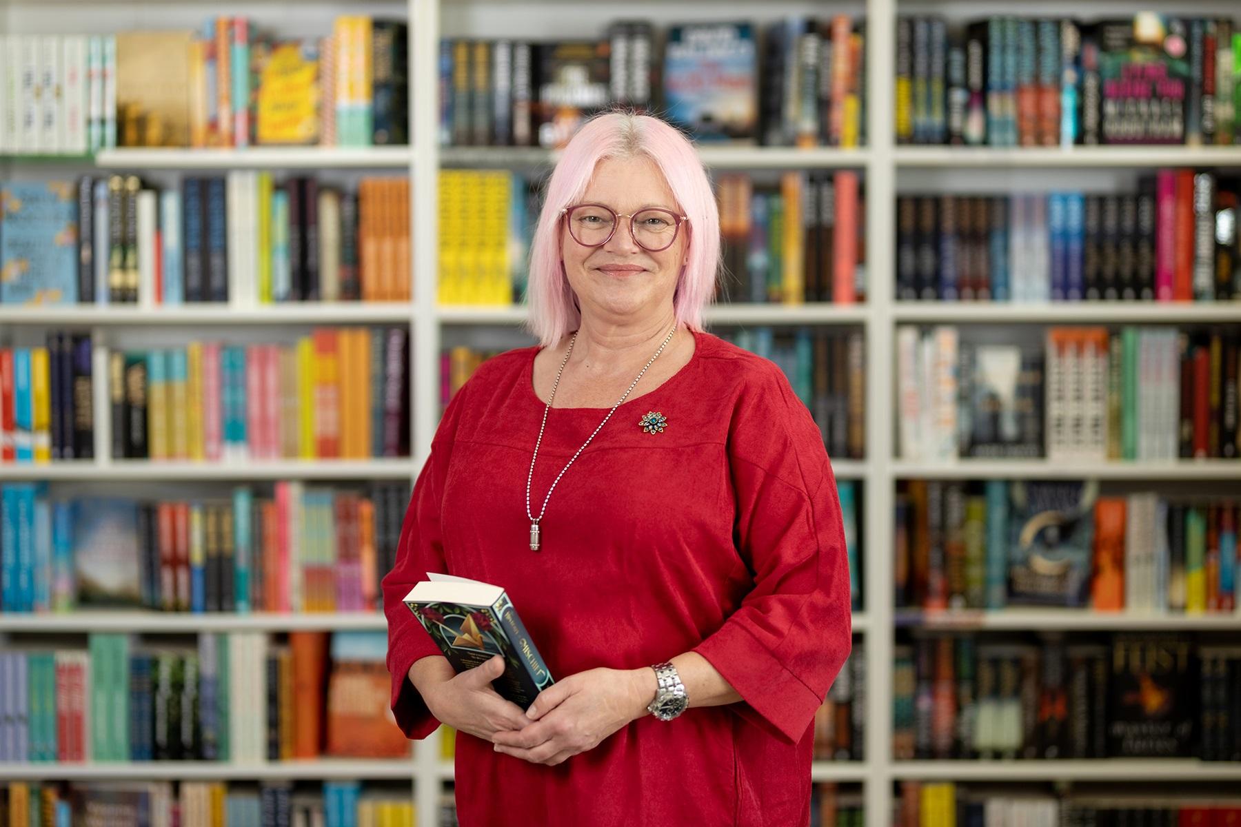 Photo of a female business owner. She is standing in her bookshop and is holding a book.