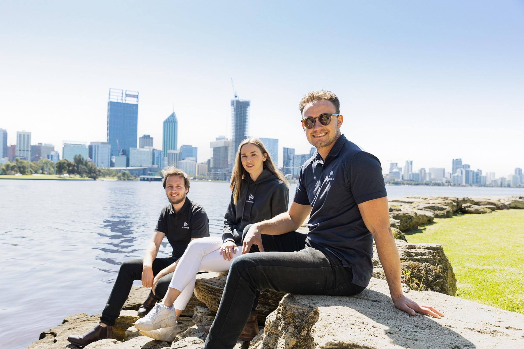 Photo of Laundon Peacock and his employees. They are sitting on the foreshore and the Perth city skyline can be seen behind them.