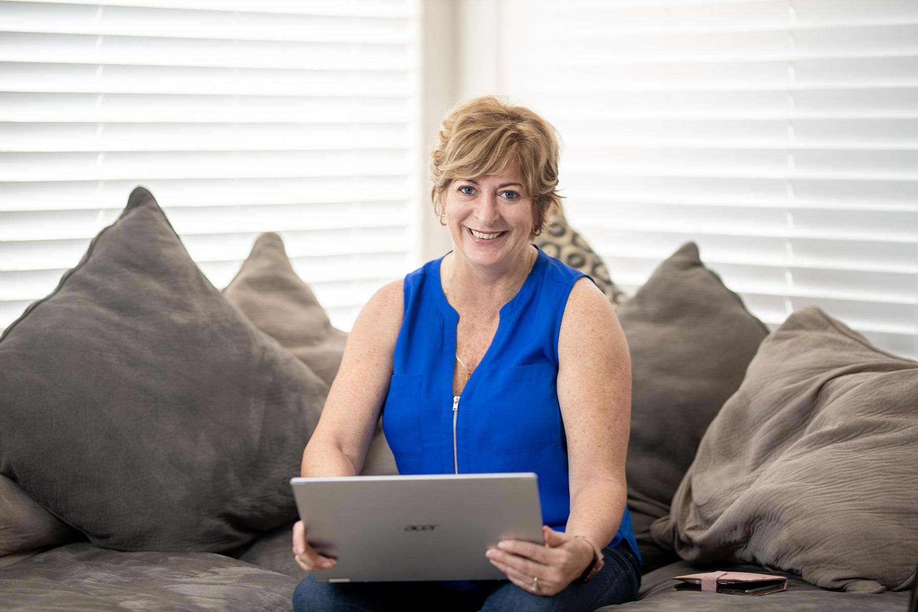 Photo of a female business owner. She is sitting on her couch at home and has a laptop in her lap.