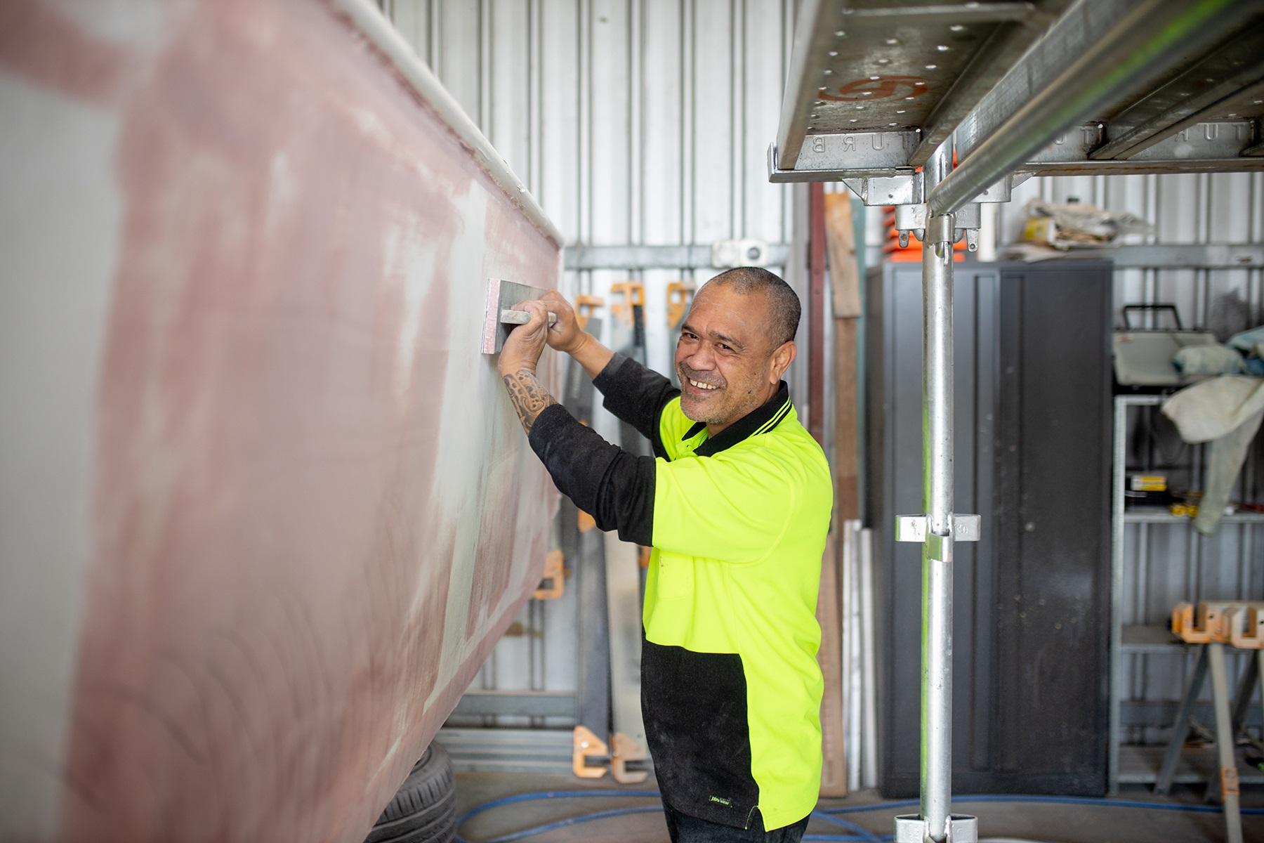Photo of a male business owner standing next to a boat that he will be repainting in his workshop.