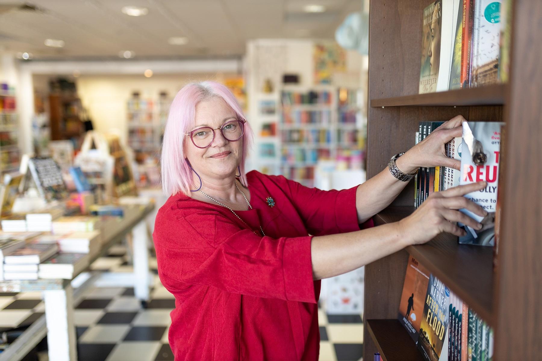 Photo of Kerry Ridley in her business My Little Bookshop. Kerry is sorting books on a book shelf.