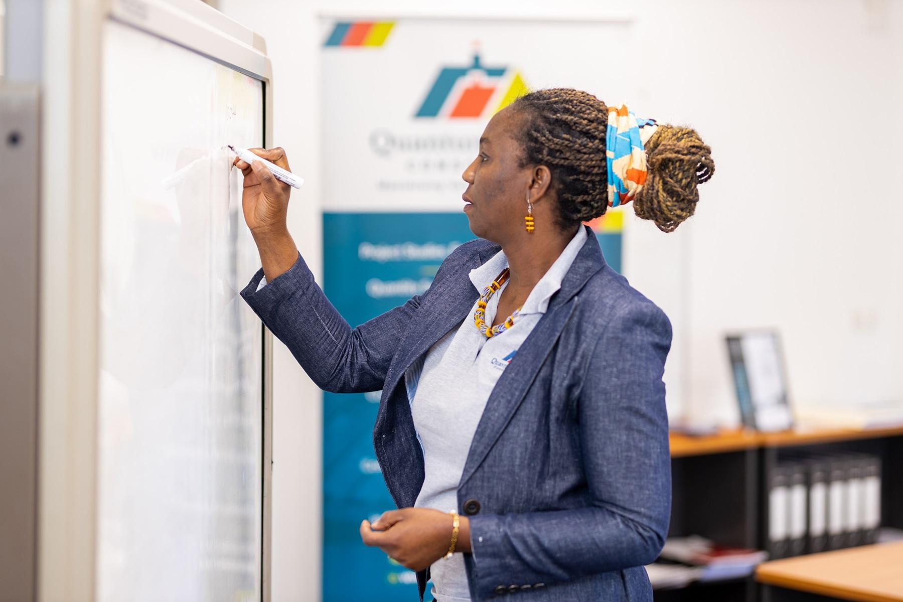Photo of a female business owner. She is writing on a whiteboard in her office.