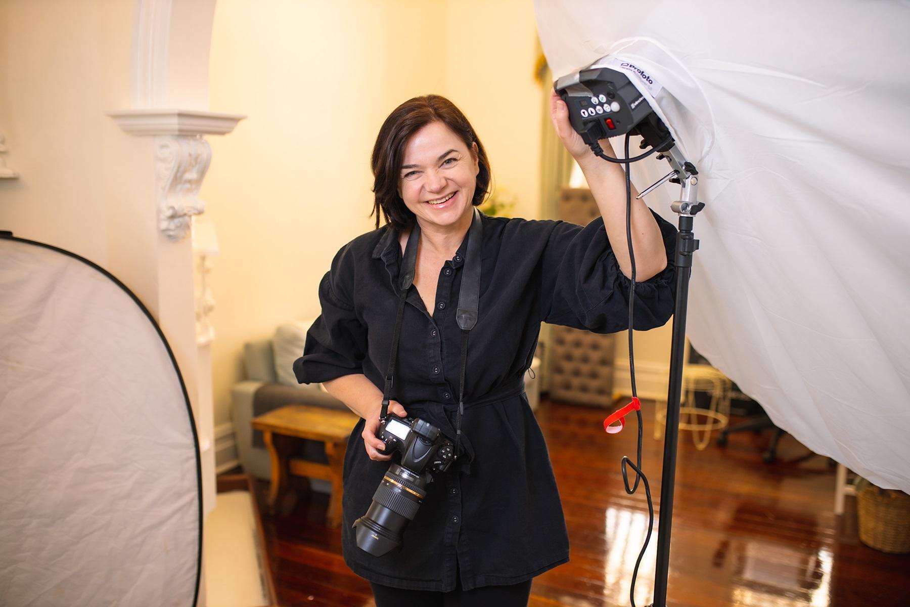 Photo of a female business owner. She is in her photography studio and is holding an SLR camera.