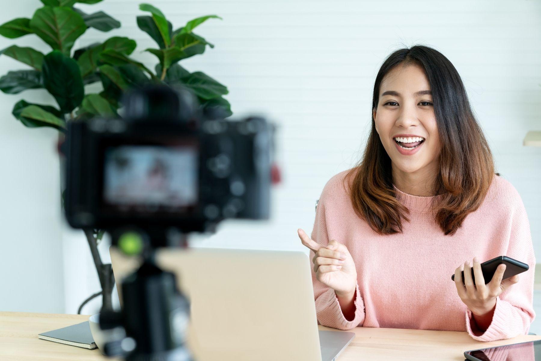 Image of  a woman smiling into a camera set up on a tripod.