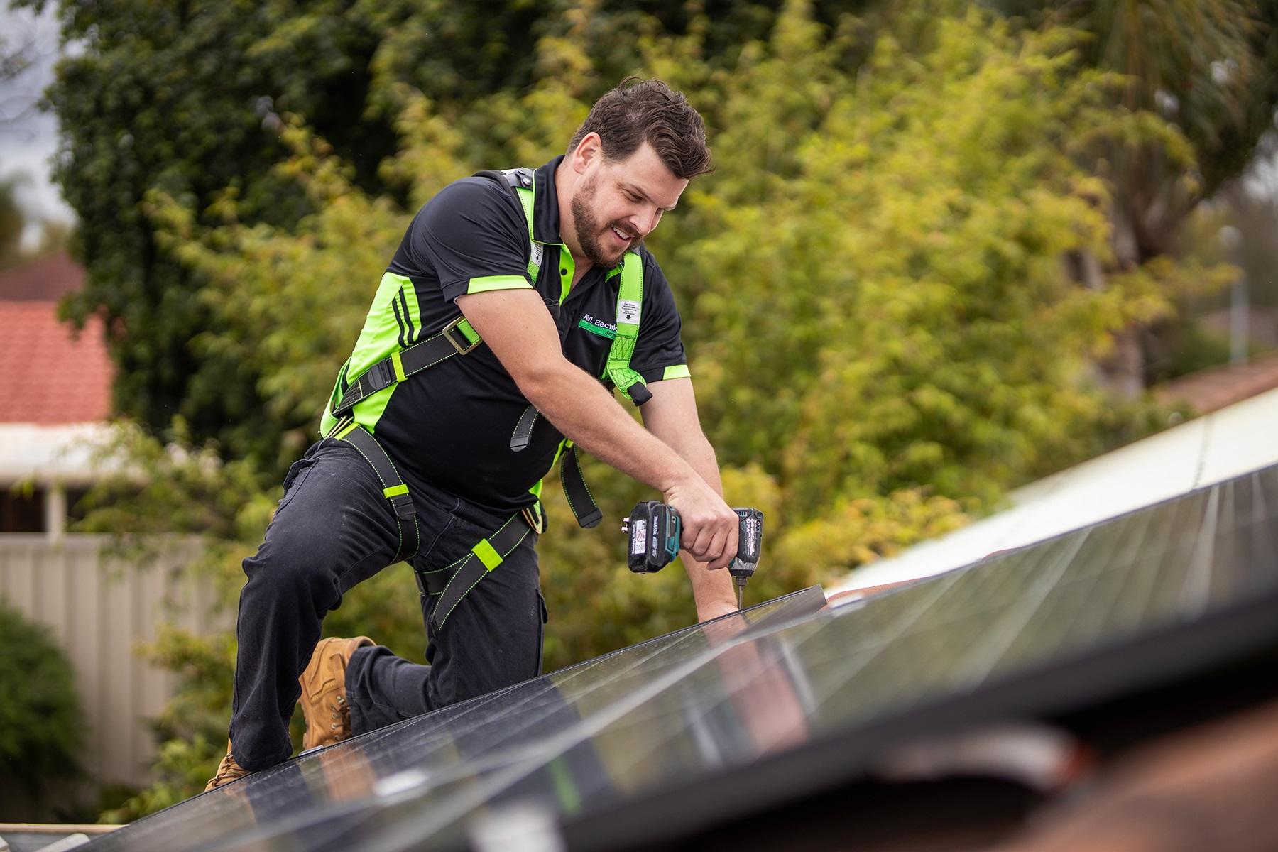 Photo of a male trades person. He is installing solar panels on a roof.