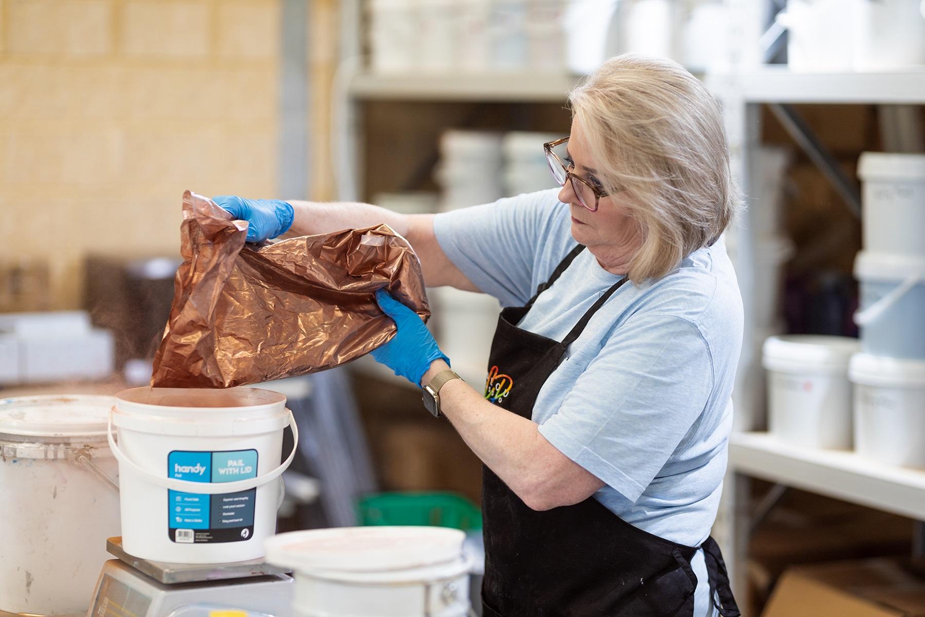 Photo of a female business owner mixing ingredients to make resin colours for artists.