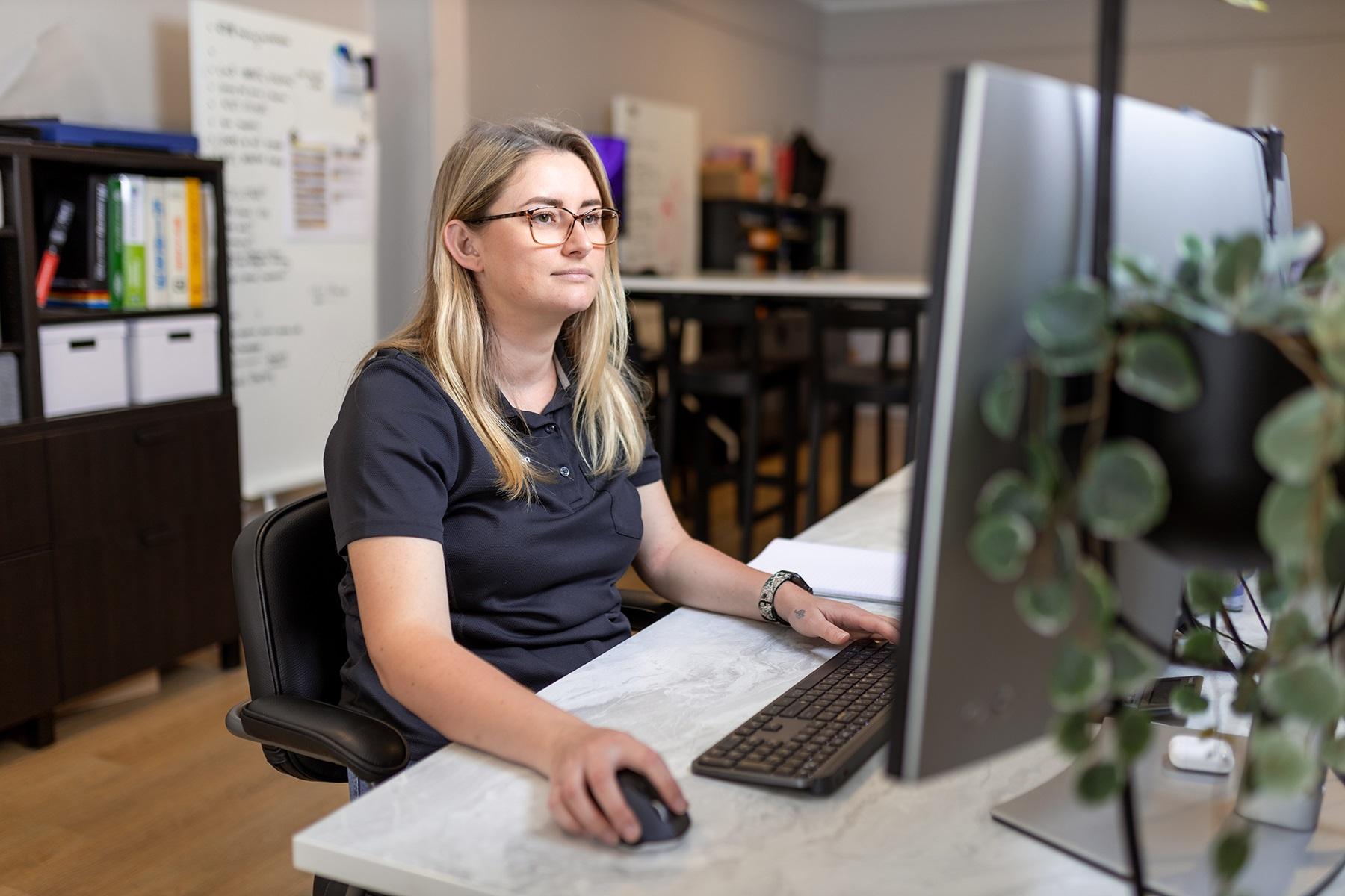 Photo of a woman sitting at a desk. She is using a computer.