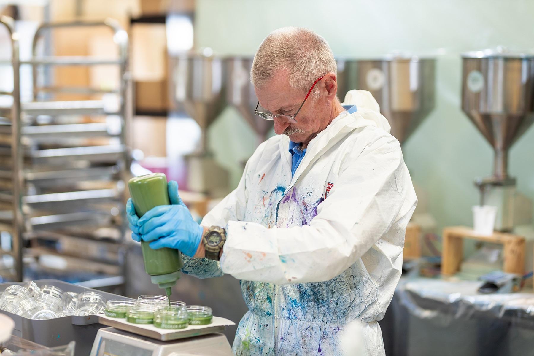Photo of a man working in a factory. He is dispensing liquid resin into jars.