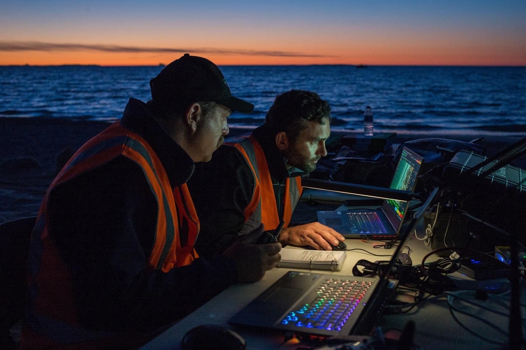 Photo of two men working on a laptop by the water as part of the Stellar Lights drone light show.