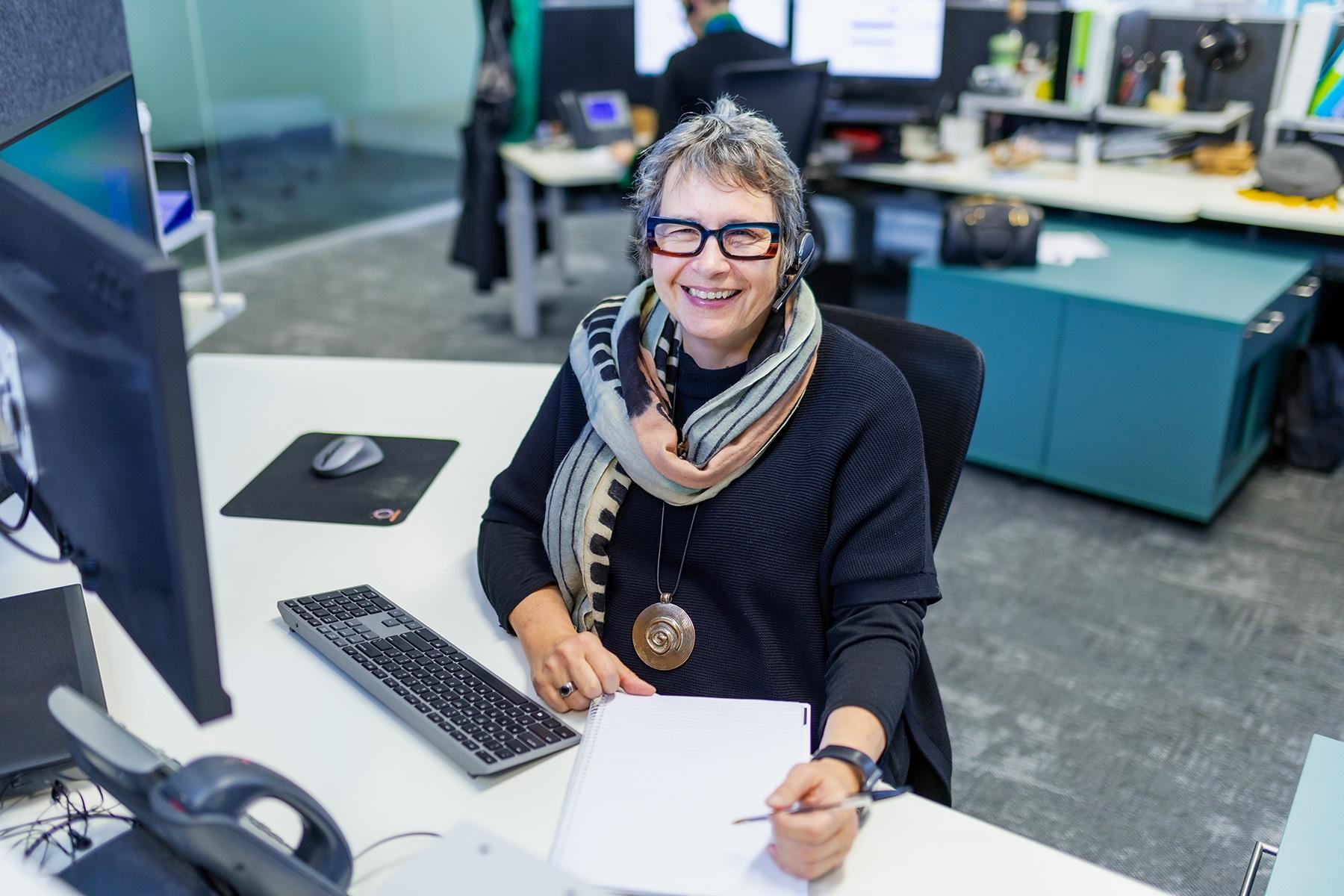 Photo of a female business adviser at the SBDC. She is sitting at her desk and smiling at the camera.
