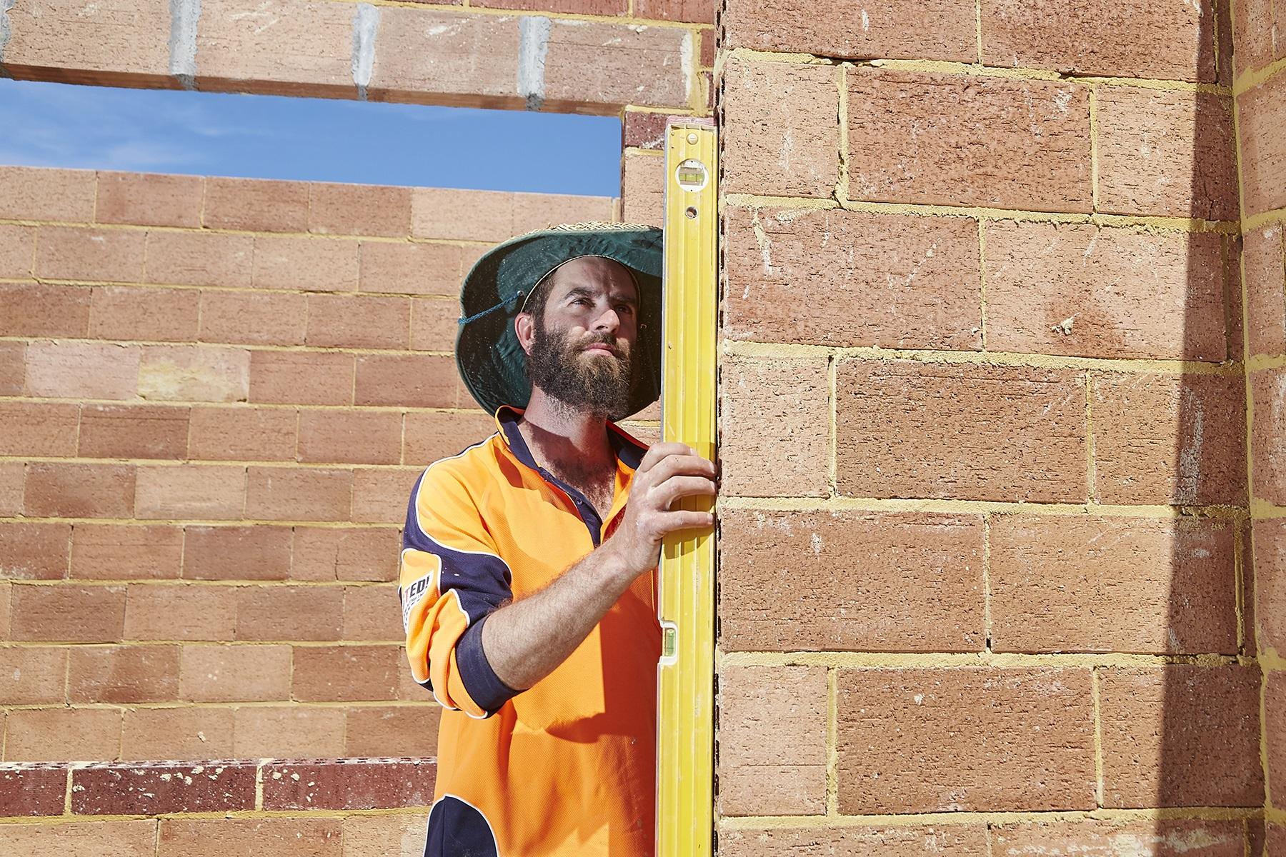 Photo of a male tradesperson checking the alignment of a brick wall during the construction of a house.