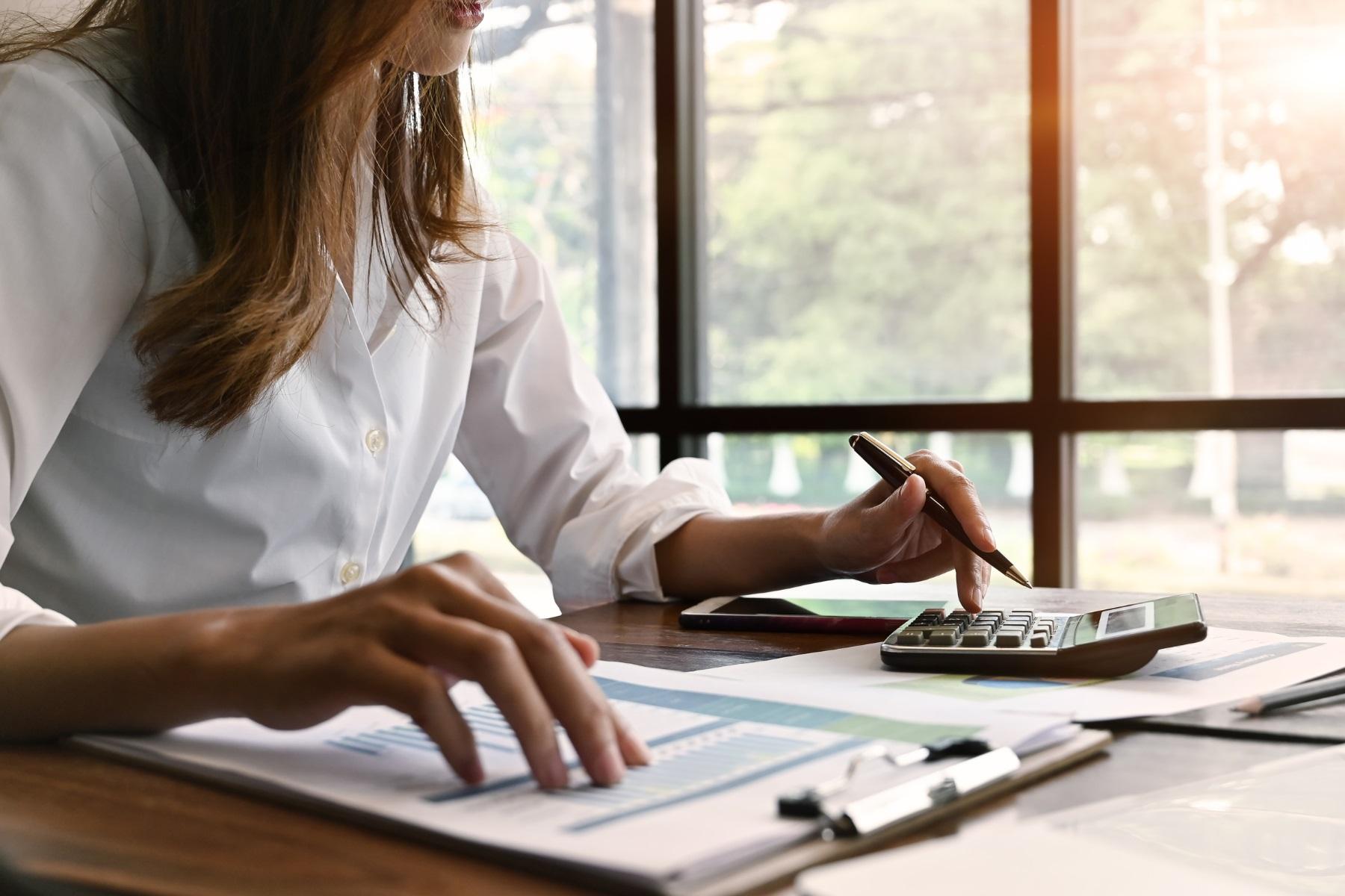 Photo of a woman sitting at a desk. She is using a calculator and reviewing financial documentation.