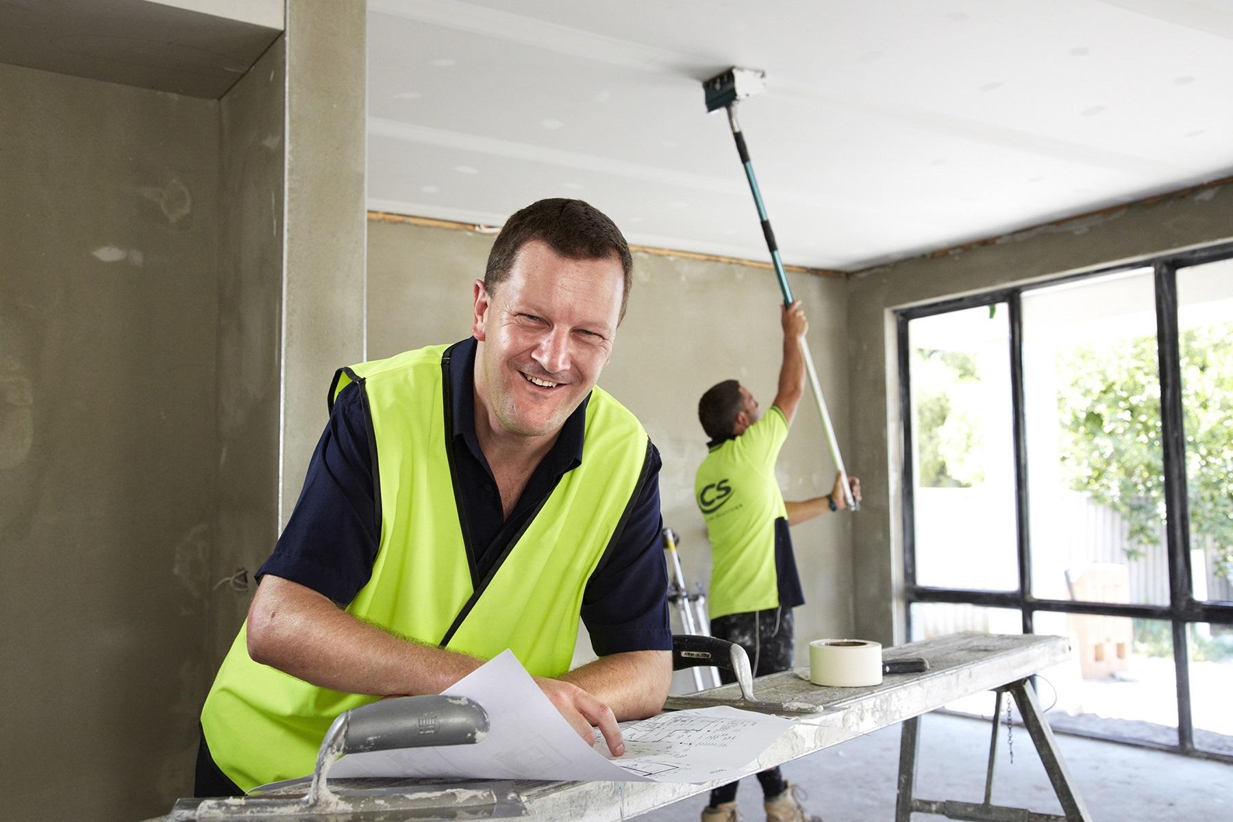Photo of two male plasterers working in a residential property. One is patching the ceiling and the other is smiling at the camera.