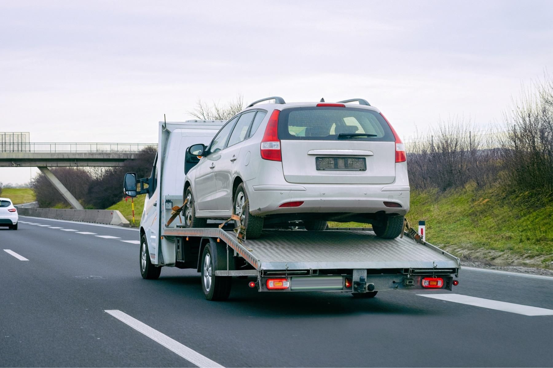 A tow truck that is towing a car along a freeway.