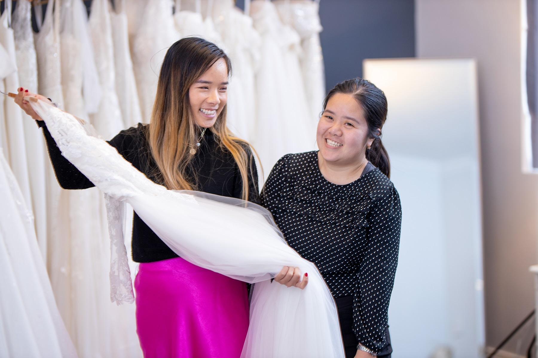 A photo of two young women in their bridal shop business. One is holding a wedding dress.