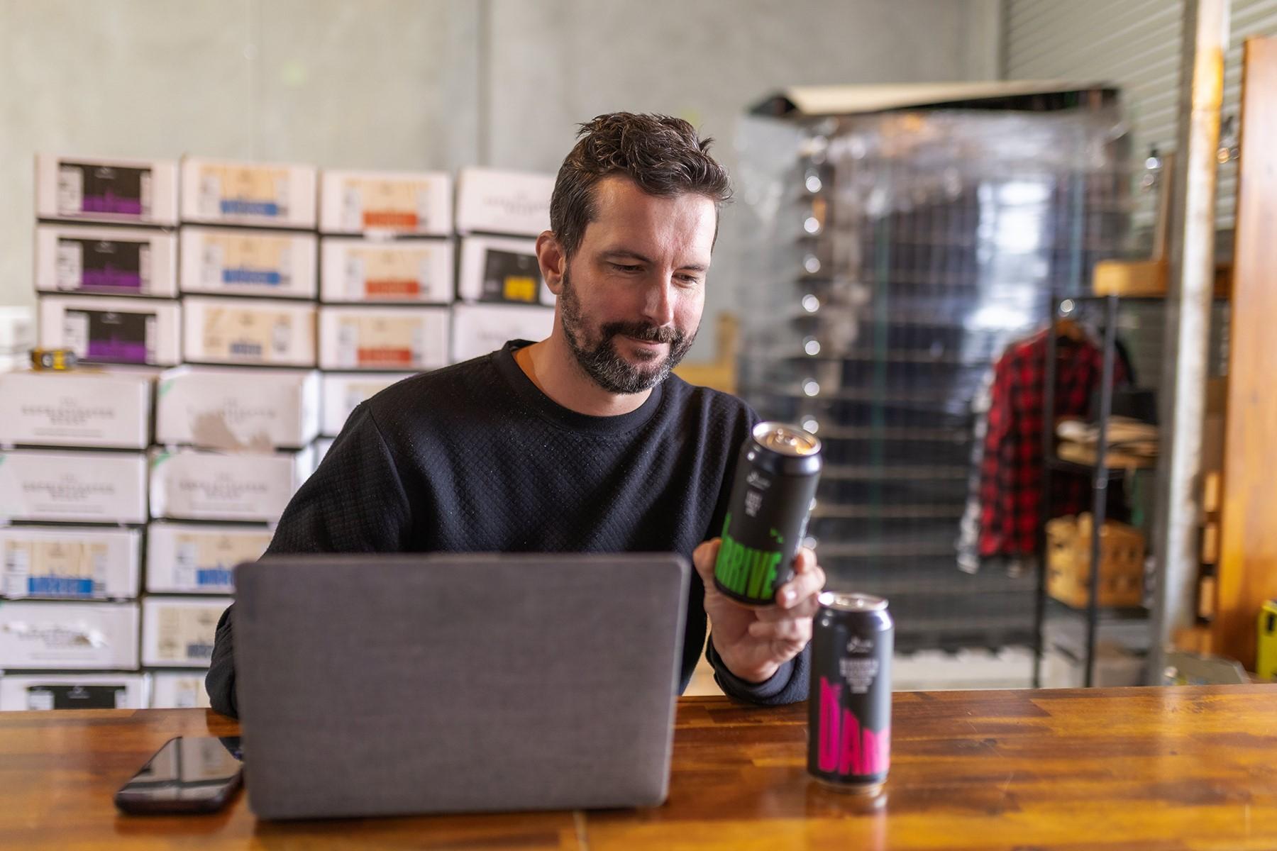 Man sitting at a counter. He is looking at an alcoholic beverage in a can.