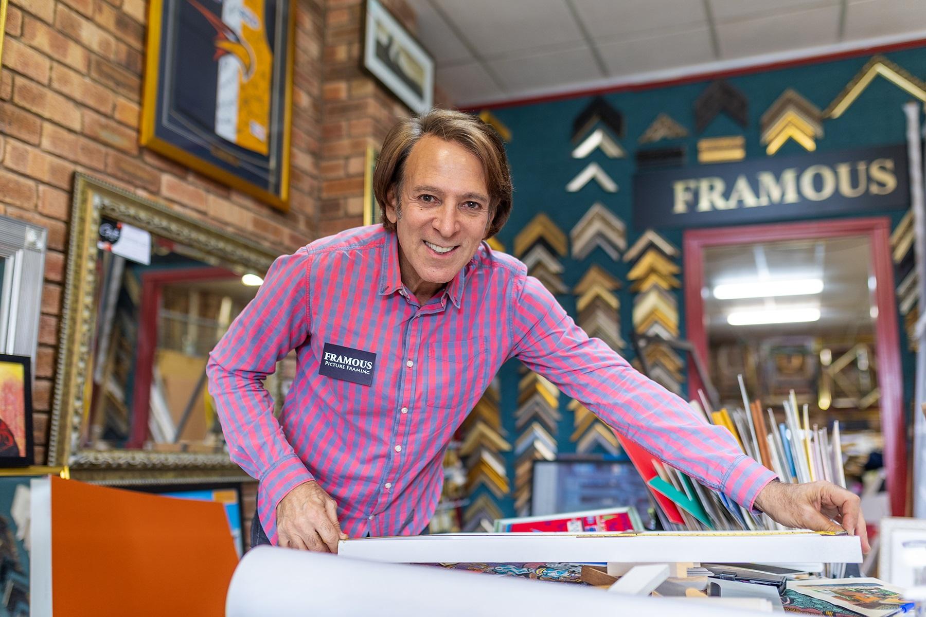 Photo of Gary Mitchell, owner of Framous Picture Framing. Gary is in his business premises measuring up an artwork for framing.