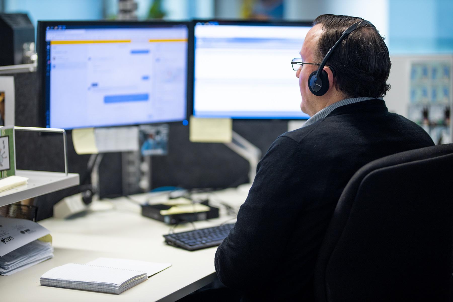 Photo of a man sitting at a computer with his back to the camera.