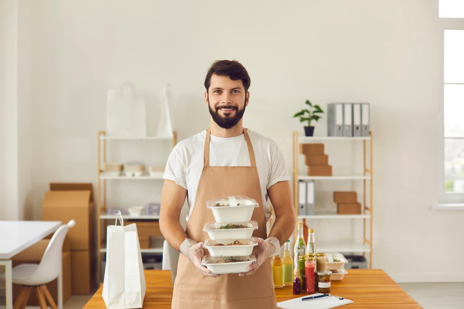 Photo of a man standing in an office. He is holding takeaway food containers.