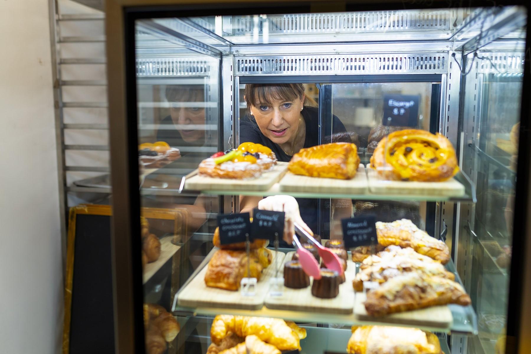 A woman using a pair of tongs to take a pastry out of a cake display cabinet.