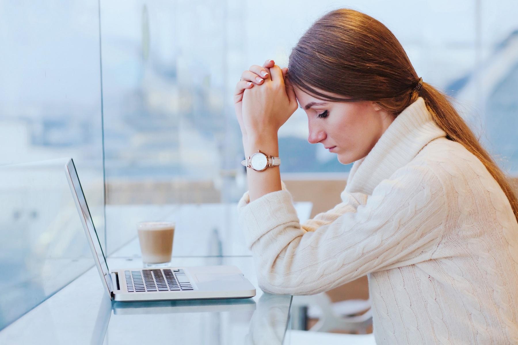 Photo of a woman sitting in front of a laptop. She has head in her hands.