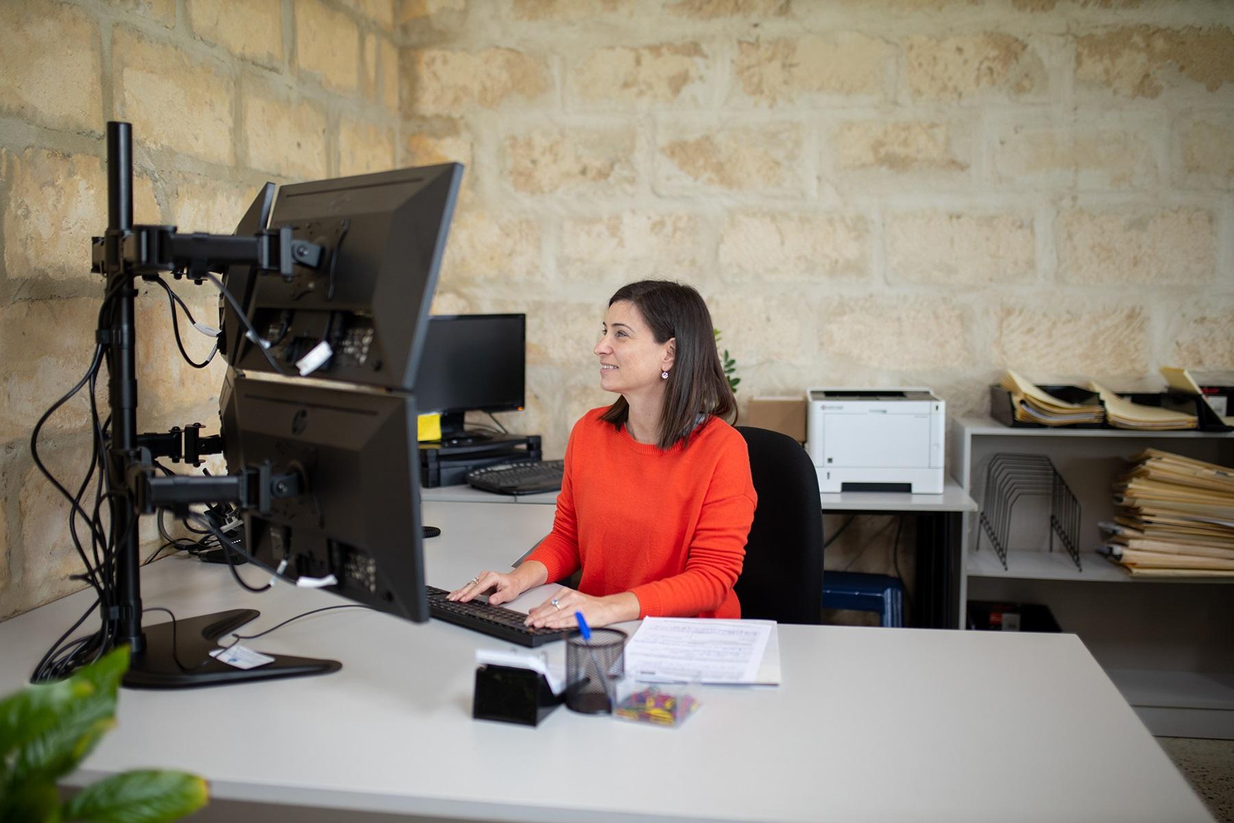Image of a lady sitting behind a desk looking at computer screens
