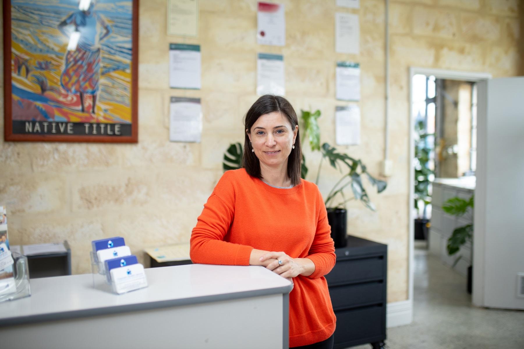 Photo of a woman leaning against a front counter in the reception area of a business.