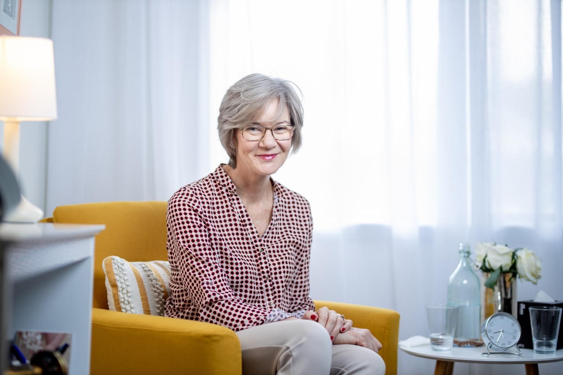 Photo of a woman sitting in an arm chair smiling at the camera.