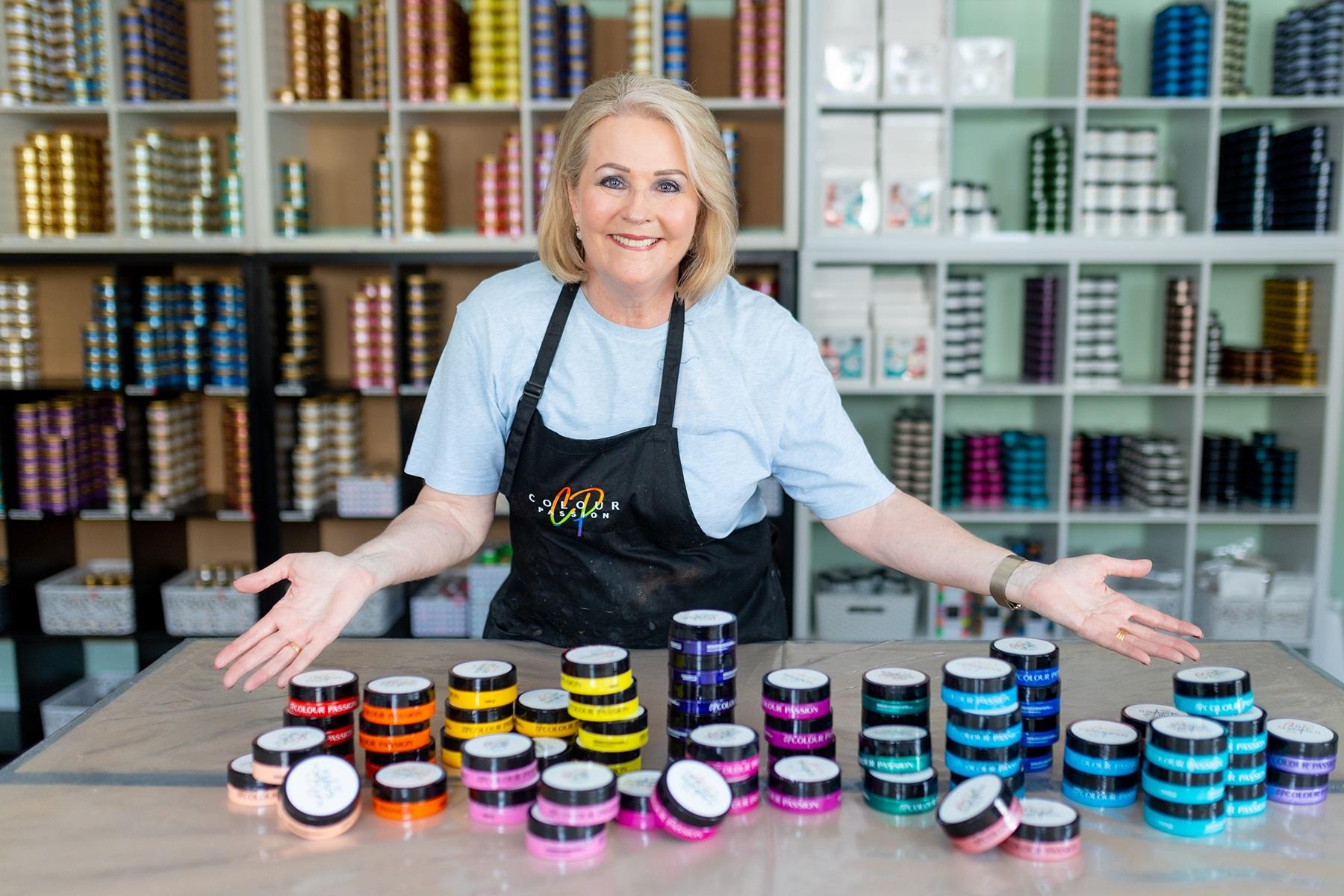 Photo of Kym Gow, owner of Colour Passion, standing in front of her range of products.