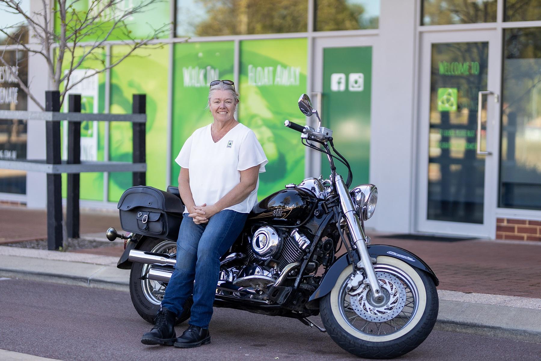 Photo of Narelle Anderson. She is sitting on a motorbike outside of The Life Spring business premises.
