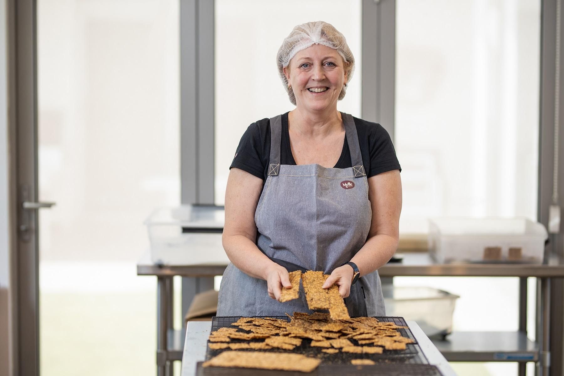 Photo of a female business owner. She is working from a production kitchen that makes cracker biscuits. 