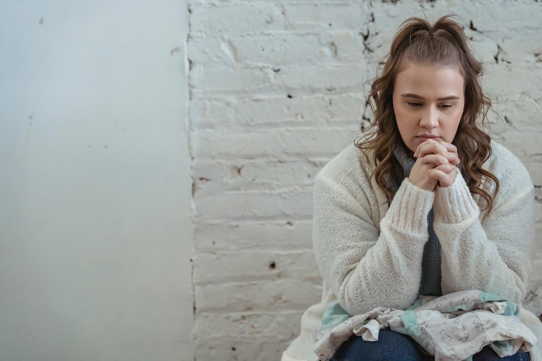 Photo of a woman. She is sitting and holding her hands up to her face.