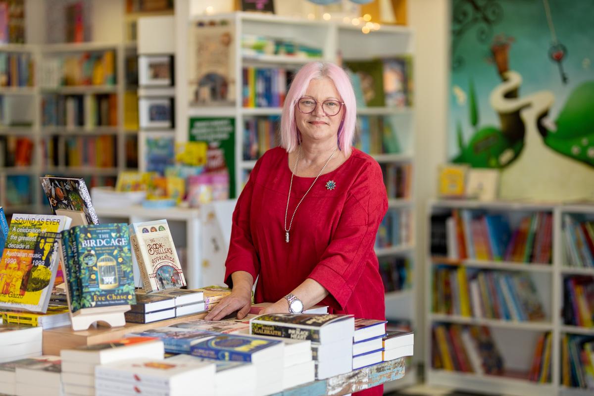 Photo of Kerry Ridley in My Little Bookshop. Kerry is standing behind a table with books displayed on it.