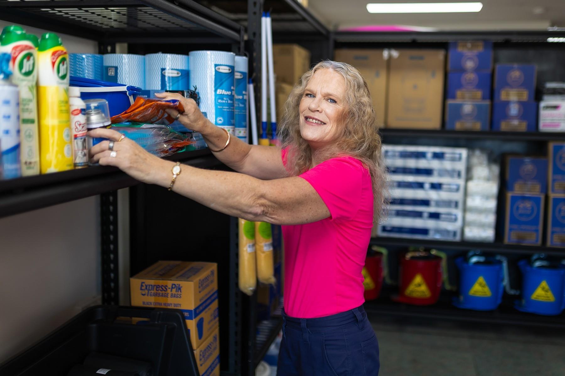 A woman arranging cleaning items on a shelving unit.