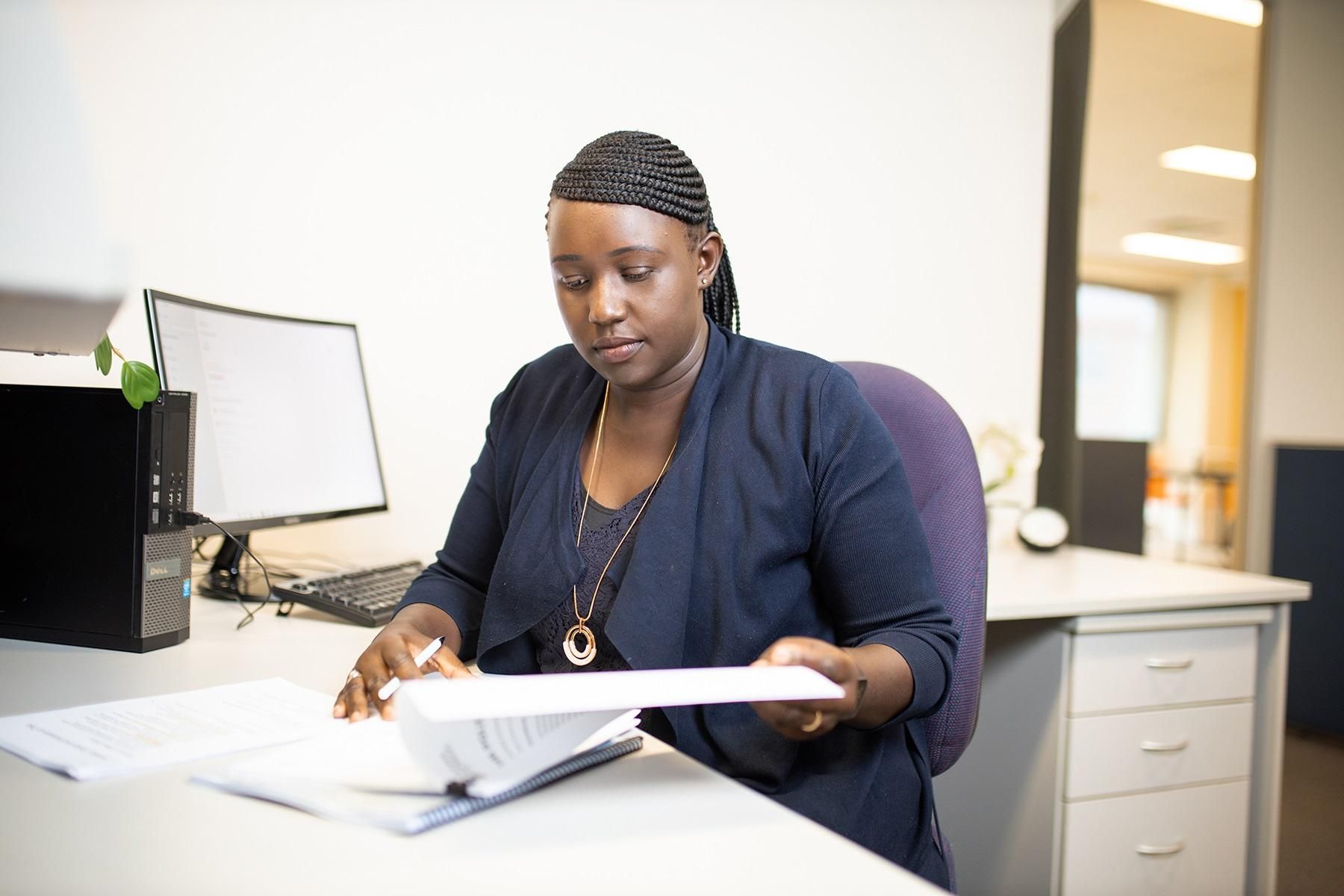 Photo of a woman sitting at a desk. She is reviewing hard copy documents.