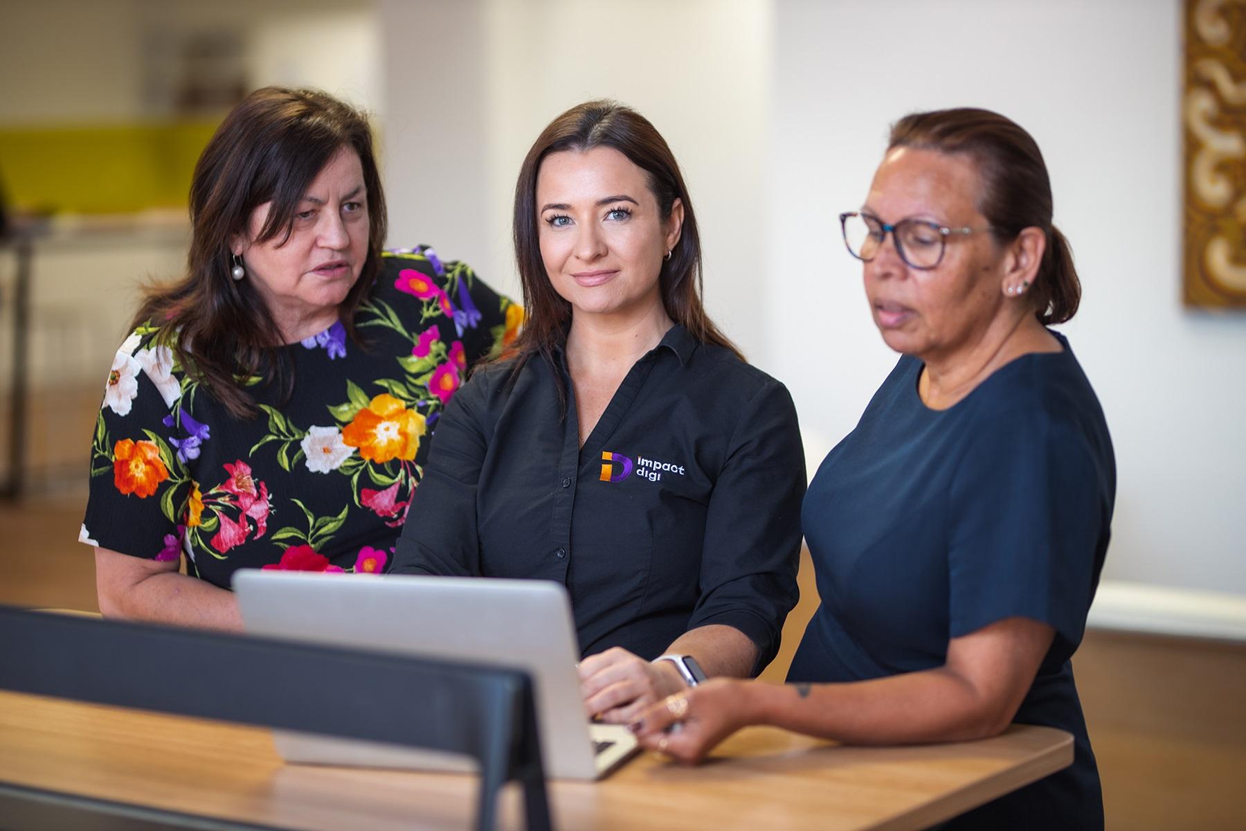A photo of a female business owner meeting with two female clients. They are standing together with a laptop.